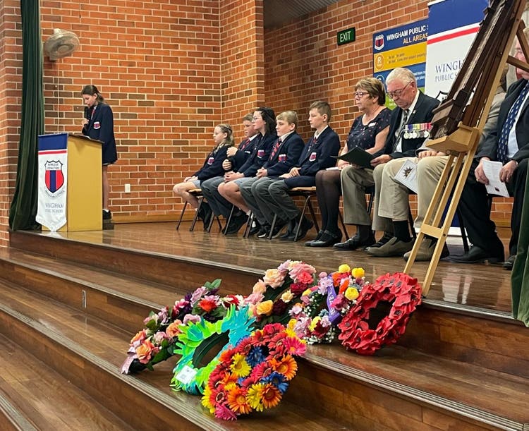 Student leaders and VIP on stage, with wreaths layed in the foreground.
